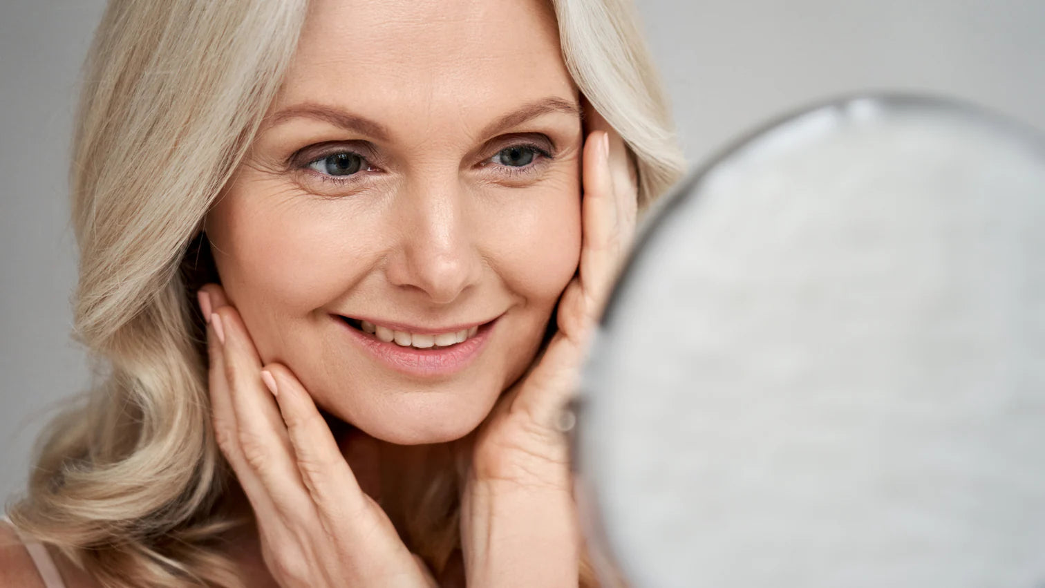 Woman examining her skin in a mirror with a neutral background